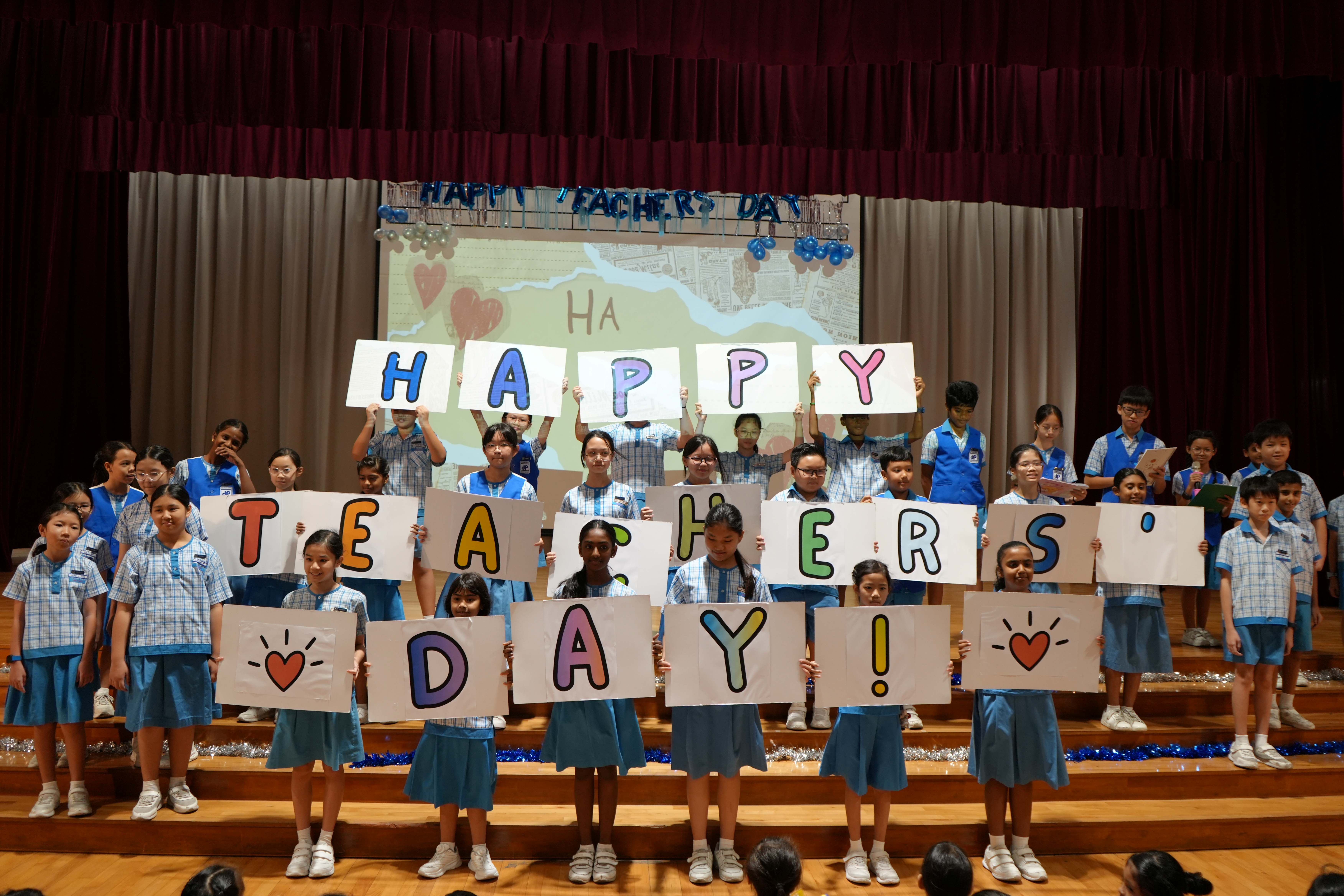 Students hold letter cards spelling “Happy Teachers’ Day” on stage